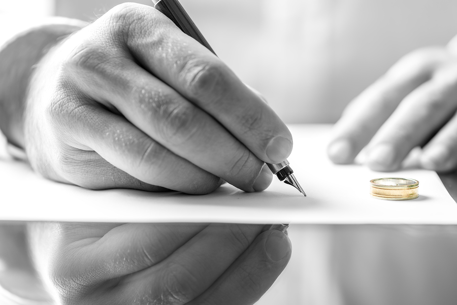 Closeup of male hand signing divorce papers.